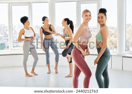group of cheerful multicultural women in sportwear chatting before pilates class, look at camera Royalty-Free Stock Photo #2440212763