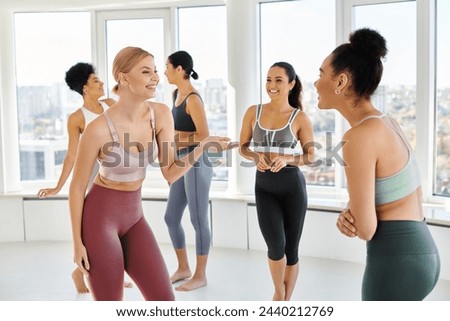 group of joyful multicultural women standing in sportwear and chatting before pilates class Royalty-Free Stock Photo #2440212769