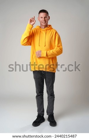 Young smiling man in casual clothes pointing up on gray wall background