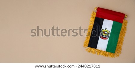 National symbol of UAE. United Arab Emirates small flag with Peregrine falcon on neutral beige background. Copy space for your text. Concept of National day Independence  Royalty-Free Stock Photo #2440217811
