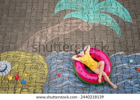 Happy little preschool girl in swimsuit on inflatable ring with sea, sand, palm painted with colorful chalks on asphalt. Cute child with having fun with chalk picture. Summer, vacations, summertime