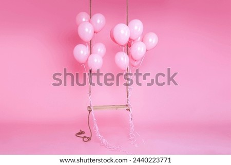 Romantic swing decorated with bunch of pink balloons on a pink background in the studio. Birthday and wedding celebration concept. Decor for holidays and events. Royalty-Free Stock Photo #2440223771