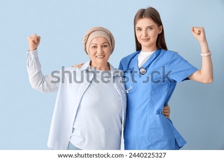 Mature woman after chemotherapy with doctor showing muscles on blue background. Stomach cancer concept