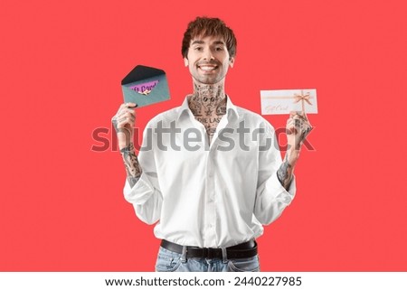 Young tattooed man with gift cards on red background