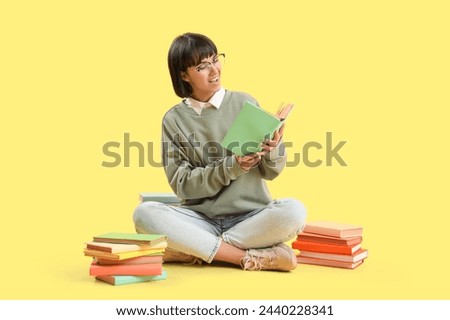 Young woman with books sitting on yellow background