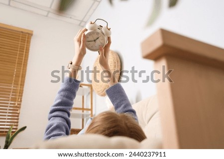 Young woman with alarm clock lying on sofa at home