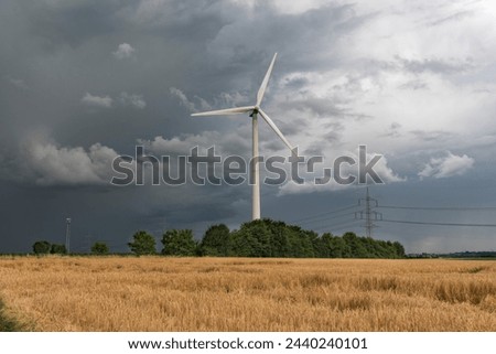 Approaching storm with gray skies passes over a wind turbine and a field with wheat