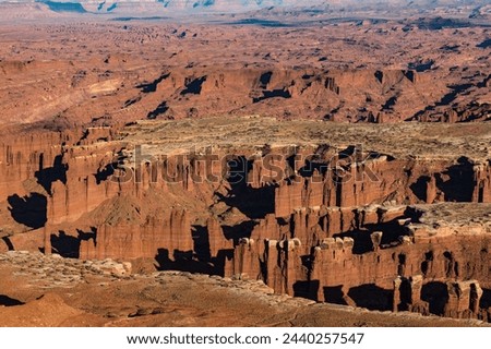 A desert landscape with a canyon in the background. The canyon is deep and wide, with a rocky terrain. The sun is setting, casting a warm glow over the landscape