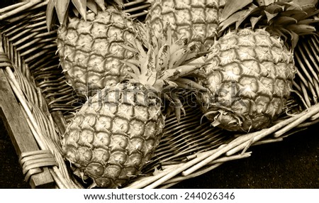 Pineapples in wicker basket at organic farmers market in Paris (France). Aged photo. Sepia.