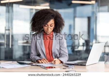 A focused professional woman immersed in her work at a well-organized office desk with a laptop and documents. Royalty-Free Stock Photo #2440265229