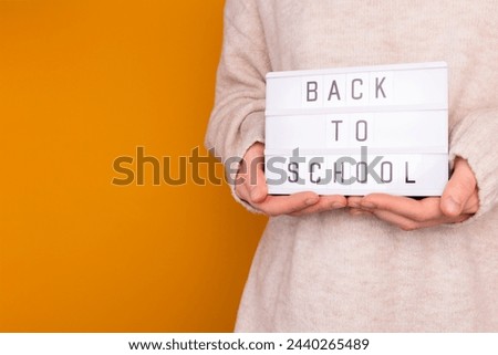 Back to school. Woman hold in hands lightbox with letters in front of yellow background. 
