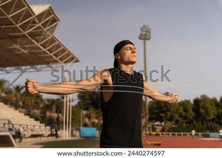 Athlete warming up before training. Stretch rubber band with arms wide open, eyes closed, facing the sun. Concept of sport and freedom. Copy space in the background Royalty-Free Stock Photo #2440274597