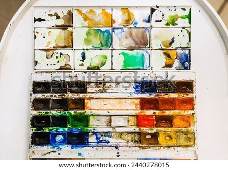 Background, texture of watercolor colored paints in disarray, in a dirty box on a white table. Photography, creativity concept, top view.