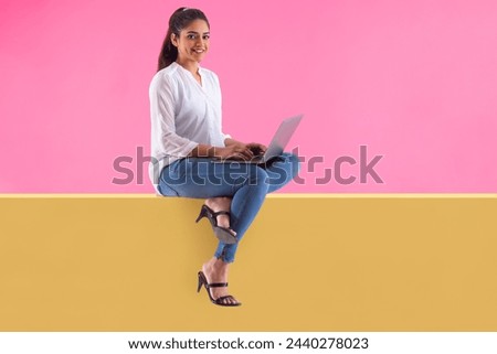 Woman with laptop on lap sitting on wall and looking at camera with smile Royalty-Free Stock Photo #2440278023