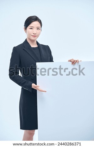 A beautiful Asian woman in a business suit is holding a white board and making various expressions and gestures.	