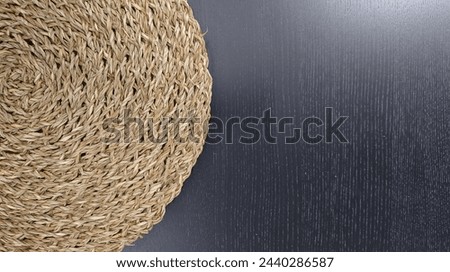Close up of a woven seashore mat on a black table, shown from above. Minimalist natural style. A closeup shot of a handwoven round straw placemat on the edge of a kitchen counter