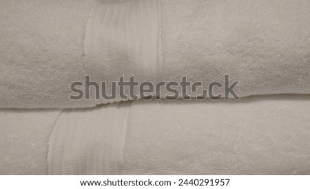 Closeup of two white towels folded on top, with the left towel slightly raised and the right neatly stacked below it. The focus is set to highlight details like creases in fabric or subtle color 
