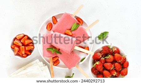 Strawberry ice cream popsicles on white plate over light stone background. Top view, flat lay 