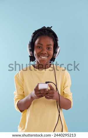 Music, phone and boy portrait with headphones in studio for internet, playlist or search on blue background. Smartphone, radio and teen model with app for podcast, streaming or sign up subscription
