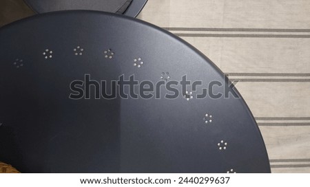An editorial home decoration photo, an aerial view from the top side angle in extreme closeup of an all gray plastic chair with small white dots on it and next to it is a dark blue round table