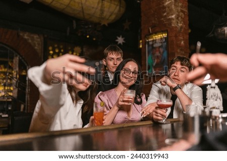 Visitors sit with delicious beverages and take pictures together at night. Bartender stirs drink at bar counter with focus on hand