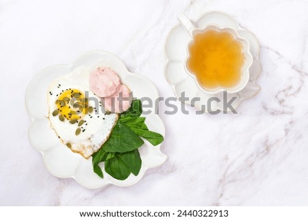 Healthy breakfast with fried egg, chicken sausage, spinach leaves, pumpkin seeds, green tea on white marble background