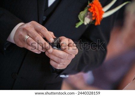 A detailed moment during a wedding ceremony where a couple exchanges rings, symbolizing their commitment. The groom's hands are carefully holding a ring box as he prepares to place the band on his