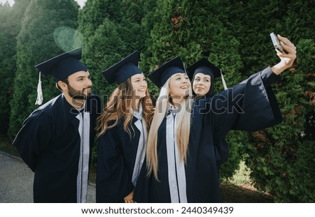 Happy students in graduation caps and gowns celebrating their achievement, taking selfies and creating memories outdoors with friends and faculty colleagues. Royalty-Free Stock Photo #2440349439