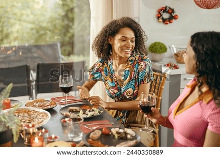 Two smiing female friends talking and drink wine during holiday party at home Royalty-Free Stock Photo #2440350889