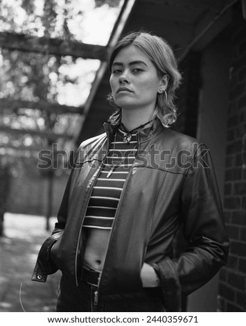 Classic portrait of strong and confident woman posing outdoors. It is a monochrome image taken with a medium format analog film camera. She in front of a building and she is wearing a leather jacket.