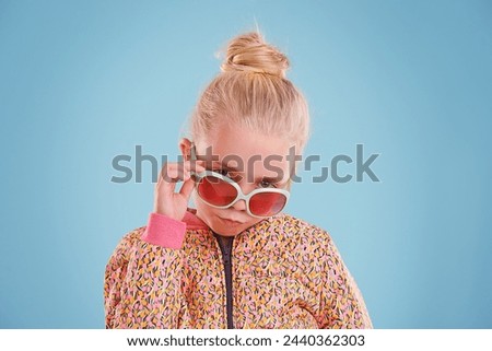 Portrait, fashion and child with sunglasses in studio with trendy, cool and funky outfit with confidence. Stylish, pout and girl kid model with cool style and accessory isolated by blue background.