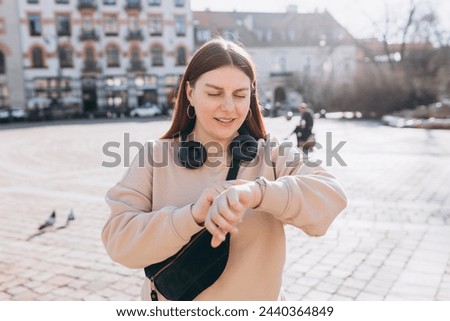 30s Beautiful young woman looking at the clock and waiting a friend or boyfriend, who is late in the street. Active lifestyle concept Royalty-Free Stock Photo #2440364849