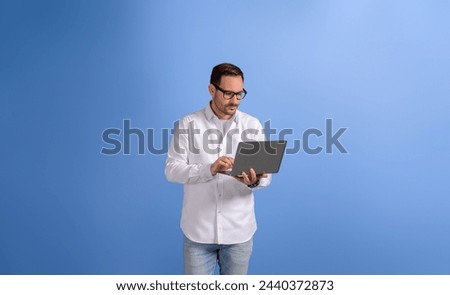 Serious handsome businessman checking e-mails over wireless computer and standing on blue background