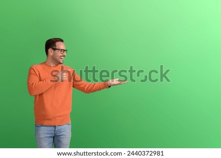 Excited young businessman pointing and advertising new product on empty palm over green background