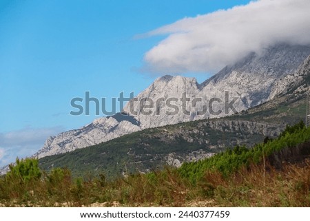 Panoramic view of cloud covered Biokovo mountain range in majestic Dinaric Alps seen from Makarska, Split-Dalmatia, Croatia, Europe. Coastline of Makarska Riviera. Hiking in the Balkans. Wanderlust Royalty-Free Stock Photo #2440377459