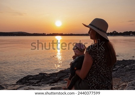 Loving mother holding small toddler enjoying romantic sunset in Medulin, Istria, Croatia, Europe. Coastline of Kvarner Gulf in Adriatic Mediterranean Sea. Dreamlike atmosphere. Family vacation concept Royalty-Free Stock Photo #2440377599