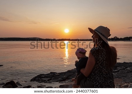 Loving mother holding small toddler enjoying romantic sunset in Medulin, Istria, Croatia, Europe. Coastline of Kvarner Gulf in Adriatic Mediterranean Sea. Dreamlike atmosphere. Family vacation concept Royalty-Free Stock Photo #2440377601