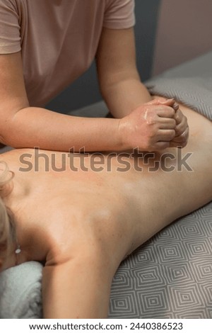 Caucasian woman undergoing manual oil massage of her back. Vertical photo.