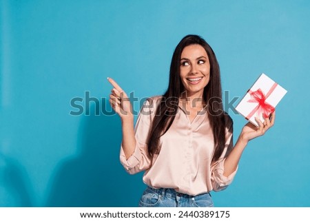 Photo of adorable woman with straight hairdo dressed silk shirt hold gift box look directing empty space isolated on blue color background