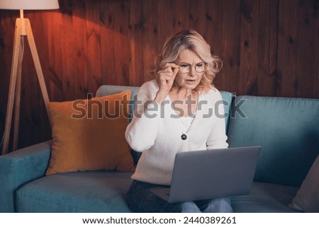 Photo of lovely retired woman sit sofa netbook read shocking news dressed casual outfit cozy home interior living room in brown warm color