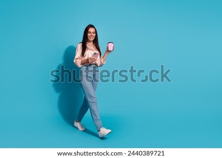 Full size photo of charming woman dressed silk shirt hold cup of cappuccino smartphone go empty space isolated on blue color background