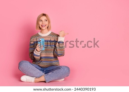 Full size photo of positive woman wear ornament pullover sit with smartphone look directing empty space isolated on pink color background