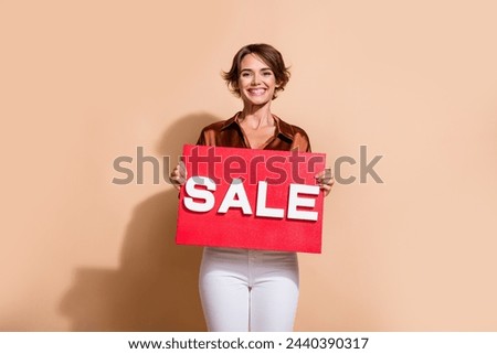Photo of cheerful positive lady dressed brown top smiling holding sale billboard isolated beige color background