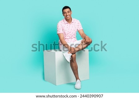 Full size photo of confident optimistic guy dressed pink polo white shorts sit on podium show shoes isolated on teal color background