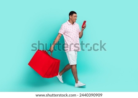 Full size photo of optimistic guy holding new outfit look at smartphone go to center empty space isolated on teal color background