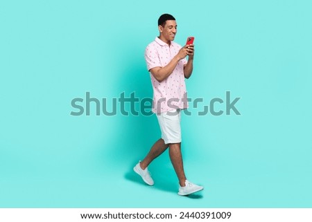Full size photo of nice guy dressed casual polo white shorts read sms on smartphone walk to empty space isolated on teal color background