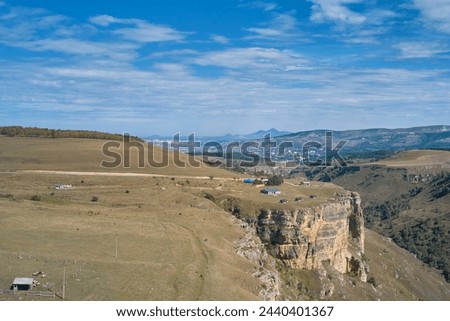 Foothills of the Greater Caucasus. Panoramic aerial view of a picturesque gorge with a farm on a rocky cliff. A populated area in the distance.