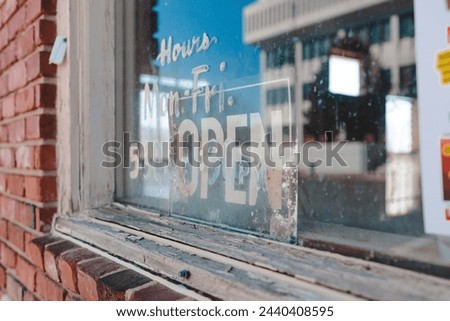 Close-up of a storefront window with an "OPEN" sign.  There is a reflection of a building in the glass. The text "HOURS" is visible on the left side of the window.