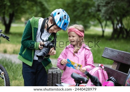 Young boy and girl looking at camera display and smiling. Brother showing picture he has taking to his younger sister. Children talking and laughing during their bicycle ride in park.