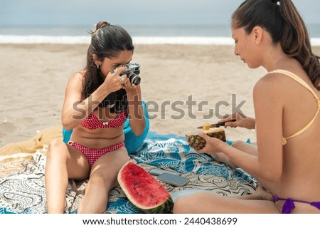Woman using analog retro camera to take pictures of holidays during a healthy picnic with a friend on the beach